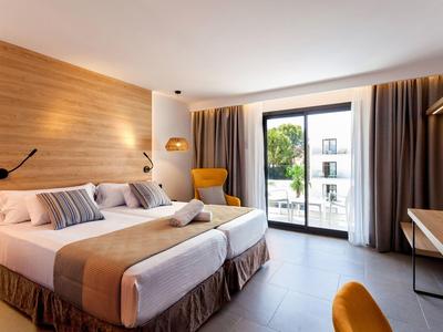Modernes Hotelzimmer mit zwei Betten, Holzwand, gelbem Sessel und großem Balkonfenster.