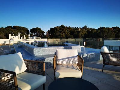 Terrassenbereich mit modernen, geflochtenen Stühlen und Glasgeländer, blauem Himmel im Hintergrund.