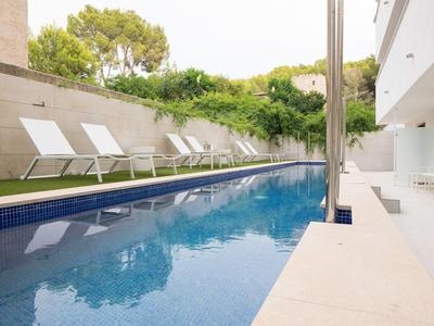 Schmaler blauer Pool neben modernem Gebäude mit weißen Liegestühlen und grünen Büschen.