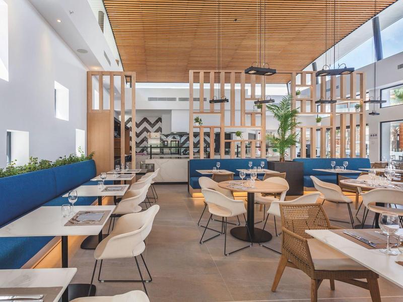 Restaurante moderno y luminoso con detalles de madera, bancos azules y grandes ventanas.