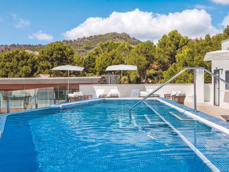 Piscina exterior agradable con tumbonas y sombrillas, rodeada de colinas verdes.