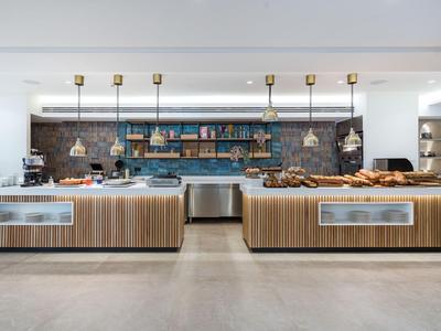Moderne Hotelküche mit Holztresen, Beleuchtung und Backwaren auf Theken.