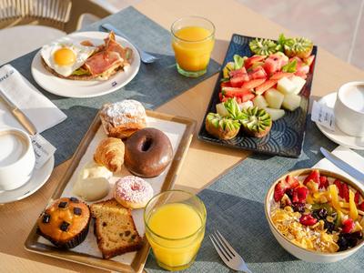 Ein gedeckter Frühstückstisch mit Orangensaft, Kaffee, Gebäck, Bagel und Obstsalat.