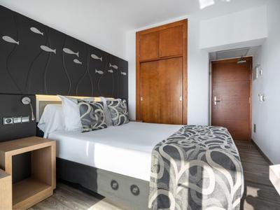 Modernes Hotelzimmer mit Doppelbett, grauem Kopfteil, Musterdecke und Holzmöbeln.