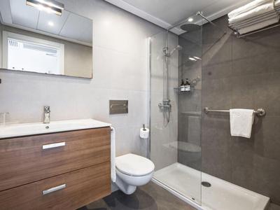 Modernes Hotelbad mit Dusche, Toilette, Waschtisch und Handtuchhalter in neutralen Farben.