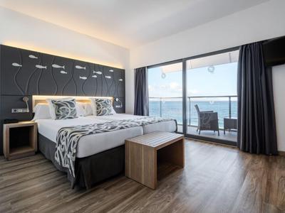 Modernes Hotelzimmer mit Bett, Holzfußboden und Balkon mit Meerblick.