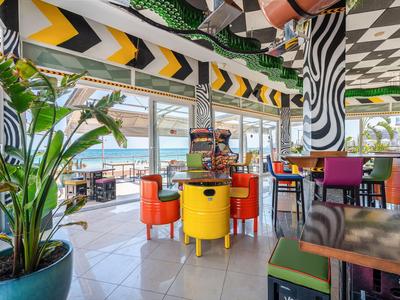 Bunt eingerichteter Hotel-Speisesaal mit Panoramafenstern und Blick auf Terrasse.