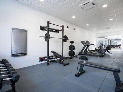 Heller Fitnessraum mit Hanteln, Kraftstationen und Cardiogeräten in modernem Hotel.
