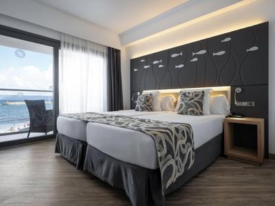 Modernes Hotelzimmer mit großem Doppelbett, dunklem Kopfteil und Balkon mit Bergblick.