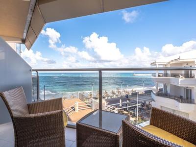Balkon mit Stühlen und Tisch, Blick auf Meer und Gebäude bei klarem Himmel.