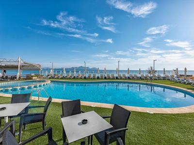 Rundes Hotelpool mit schwarzen Stühlen und Tischen auf grünem Rasen, Meerblick im Hintergrund.