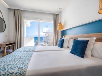 Helles Hotelzimmer mit Doppelbett, blauen Akzenten und Terrasse mit Meerblick.