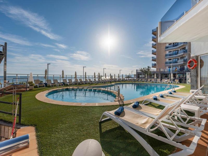 Buitenzwembad met ligstoelen, gras en uitzicht op de oceaan onder een heldere lucht.