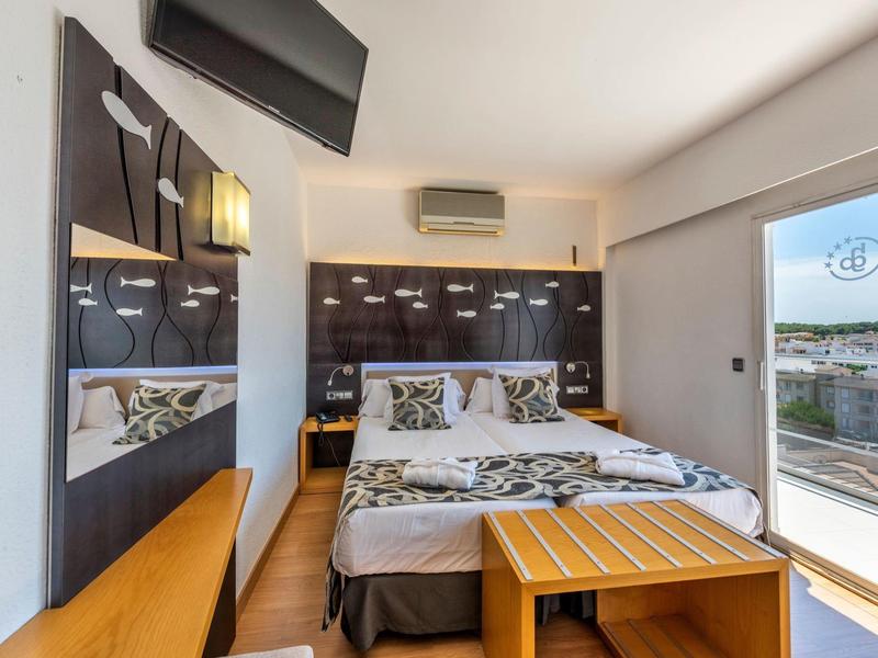 Moderne hotelkamer met tweepersoonsbed, sierkussens, houten meubels en balkonuitzicht.