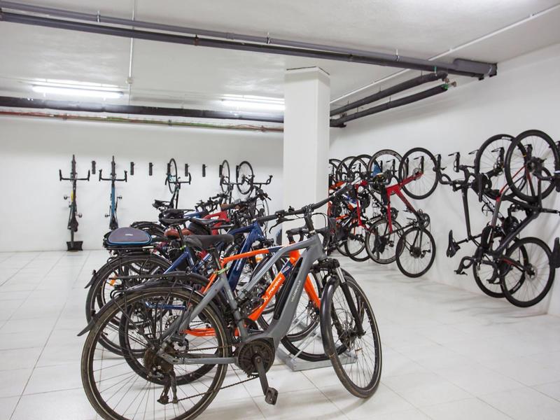 Binnenfietsenstalling met diverse fietsen, sommige aan de muur gehangen, in een schone witte ruimte.