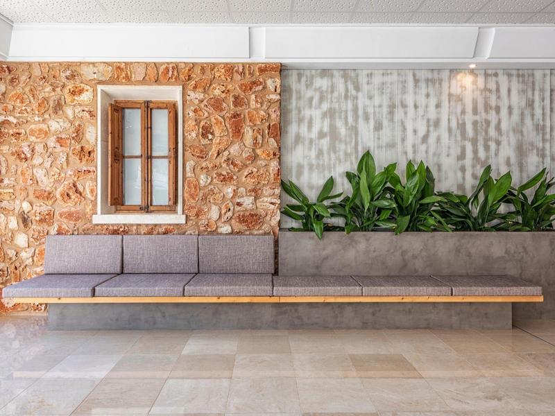 Moderne hotel lobby met grijze bank, houten wandpaneel, groene planten en betegelde vloer.