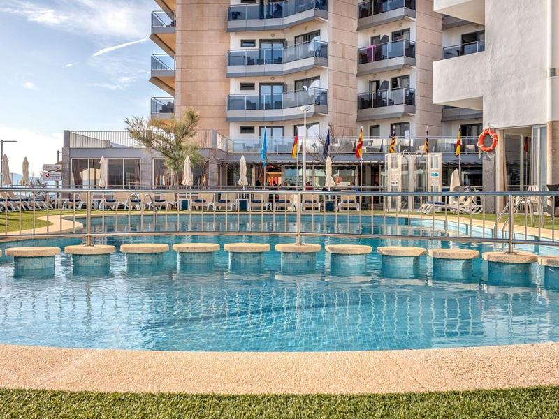 Rond buitenzwembad met hekken in een hotellentuin onder een zonnige lucht.