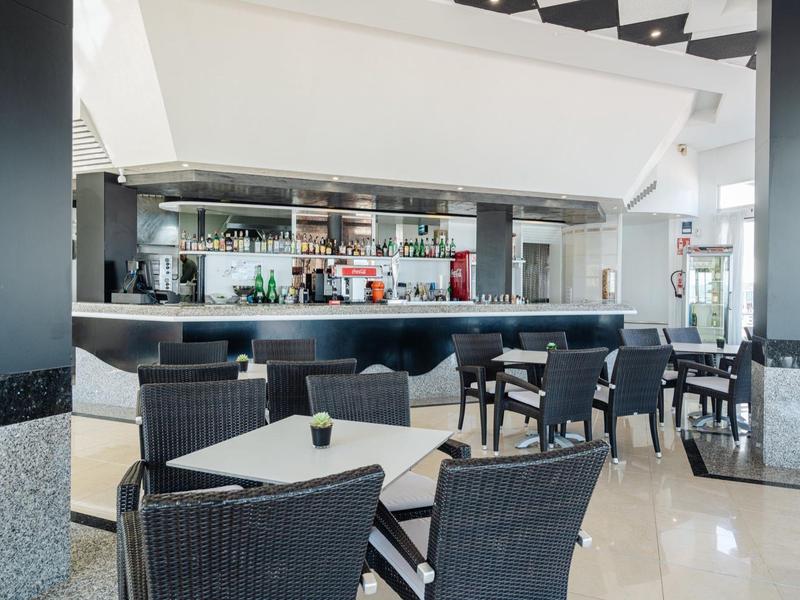 Moderne hotel lounge met zwarte stoelen, witte tafels en een goed gevulde bar onder een wit plafond.