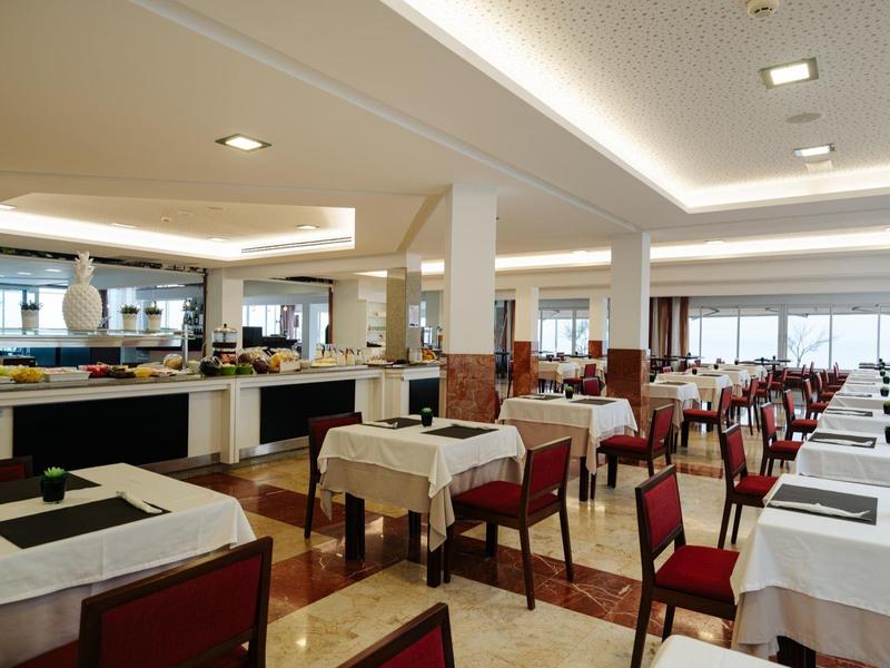 Riante hotel eetzaal met witte tafelkleden en rood gevoerde stoelen.