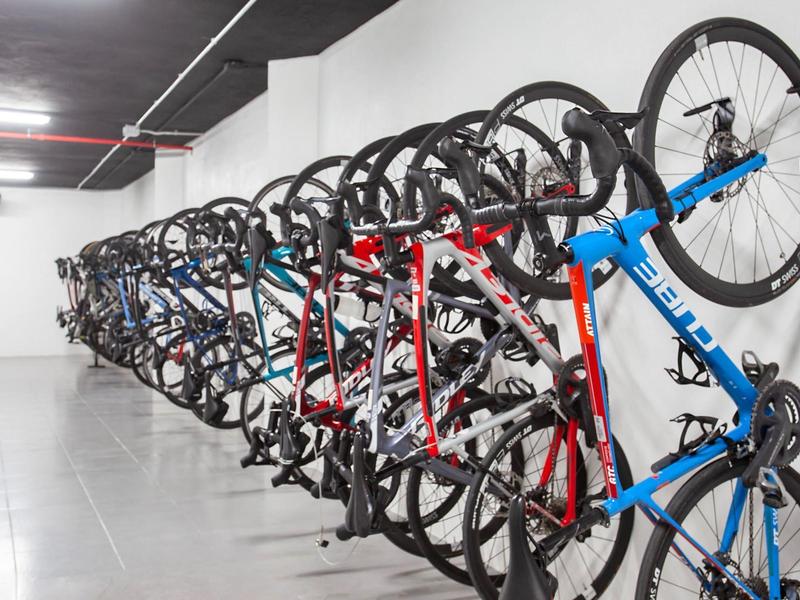 Lange rij fietsen verticaal geparkeerd in een opslagruimte met witte muren en grijze vloer.