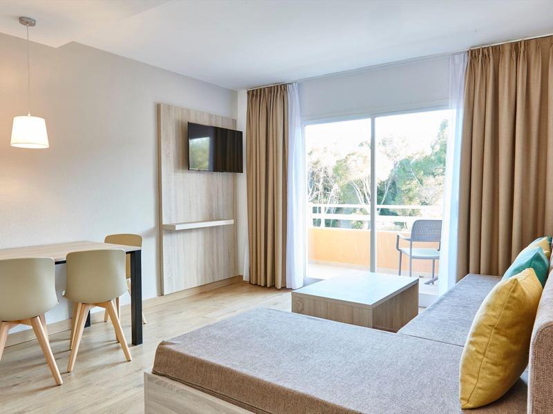 Chambre d'hôtel moderne avec canapé, télévision et balcon donnant sur un jardin.