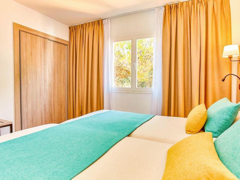 Chambre d'hôtel lumineuse avec lit double, rideaux jaunes et accents turquoise.