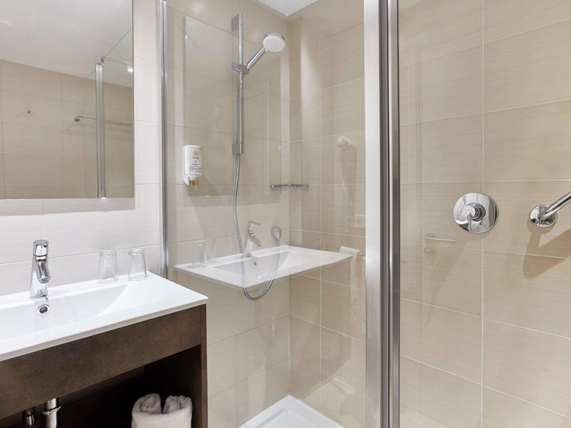 Coin douche moderne avec cloison en verre, lavabo et murs carrelés beiges.