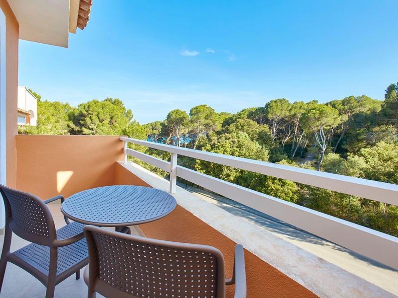 Balcon avec deux chaises et une table avec vue sur des arbres verts sous un ciel bleu.