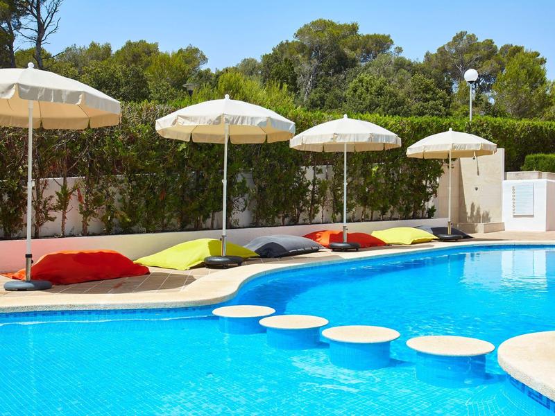 Piscine avec parasols et coussins colorés dans un espace extérieur ensoleillé.