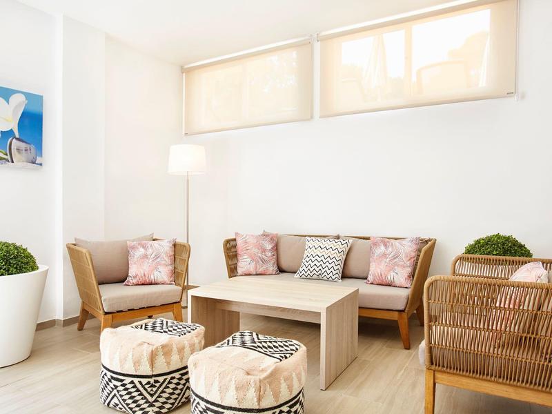 Salon lumineux avec canapé, fauteuils, table basse et coussins décoratifs aux tons neutres.