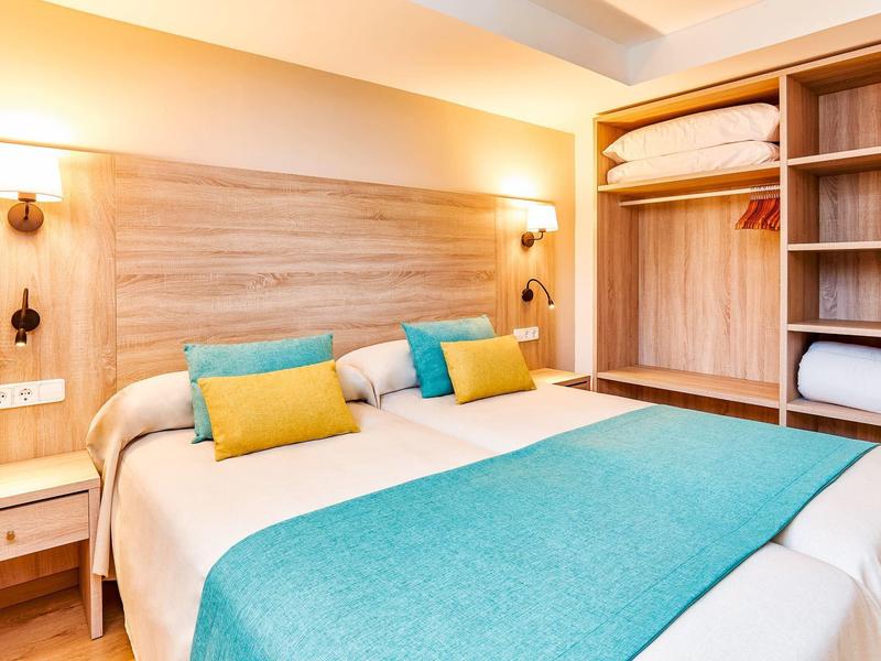 Chambre d'hôtel moderne avec lit double, coussins colorés et armoire en bois ouverte.