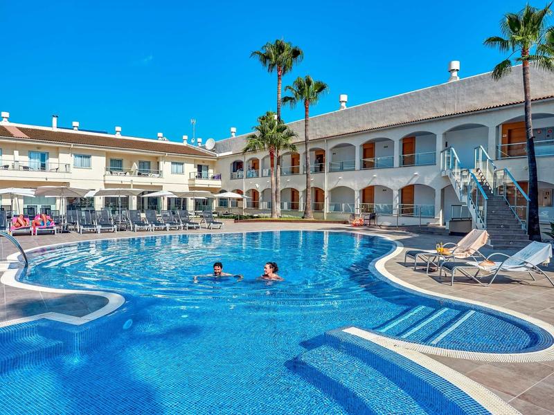 Basen na zewnątrz hotelu z palmami i leżakami.