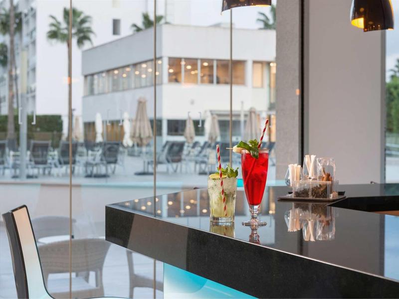 Elegancki bar z kolorowymi napojami, widokiem na basen i palmy na zewnątrz.