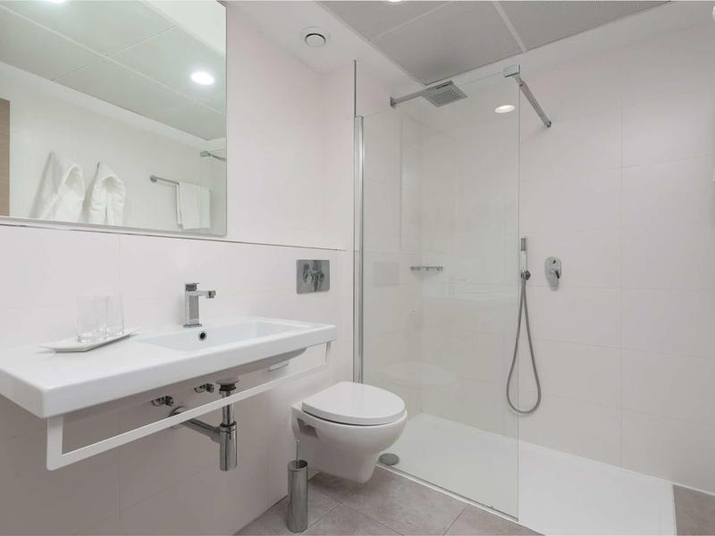 Nowoczesna łazienka z prysznicem bez brodzika, białą umywalką i wiszącą toaletą.