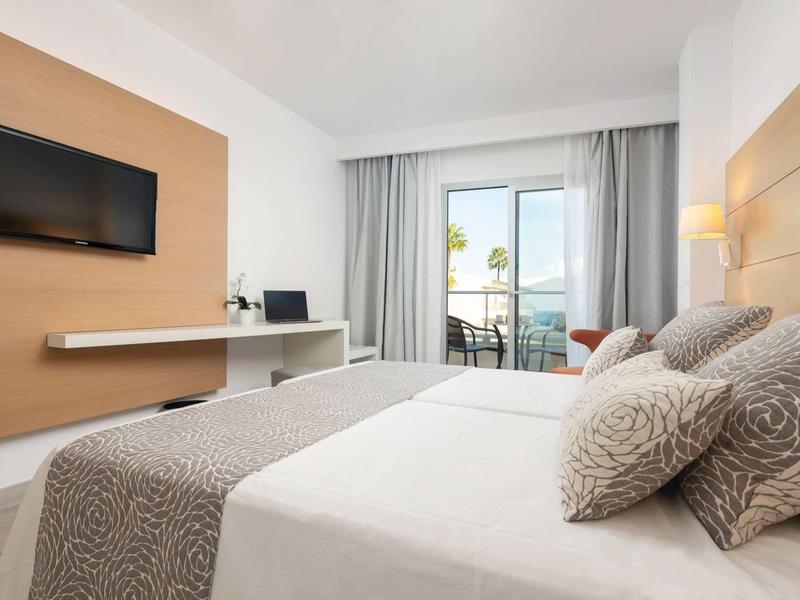 Nowoczesny pokój hotelowy z podwójnym łóżkiem, telewizorem na ścianie i balkonem z widokiem.