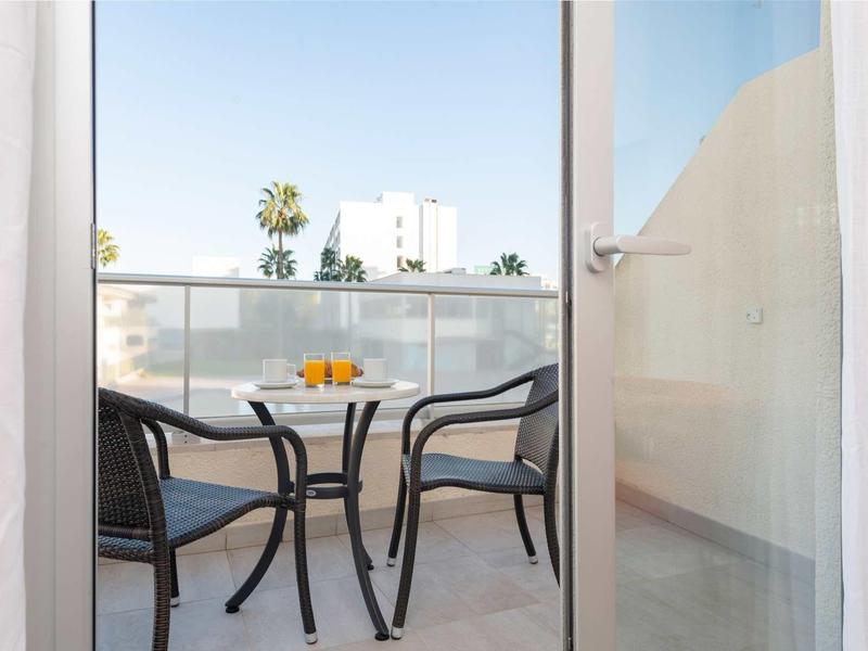 Taras hotelowy z stołem i krzesłami, widok na palmy i biały budynek.