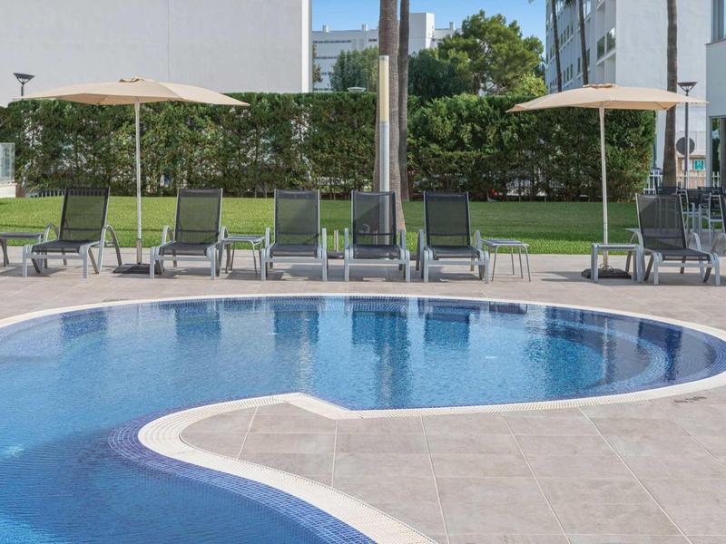 Basen na zewnątrz z leżakami i parasolami w nowoczesnym, zielonym otoczeniu.