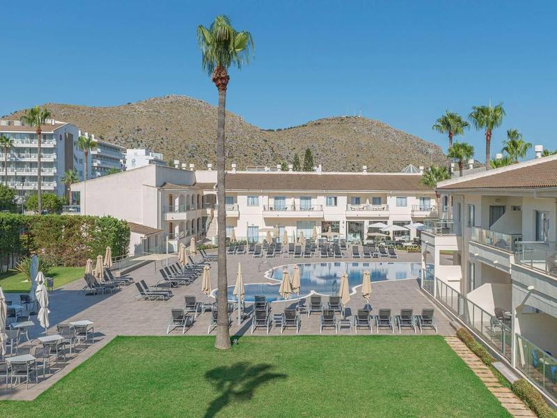 Basen na zewnątrz z leżakami i budynkami hotelowymi pod jasnym niebem.