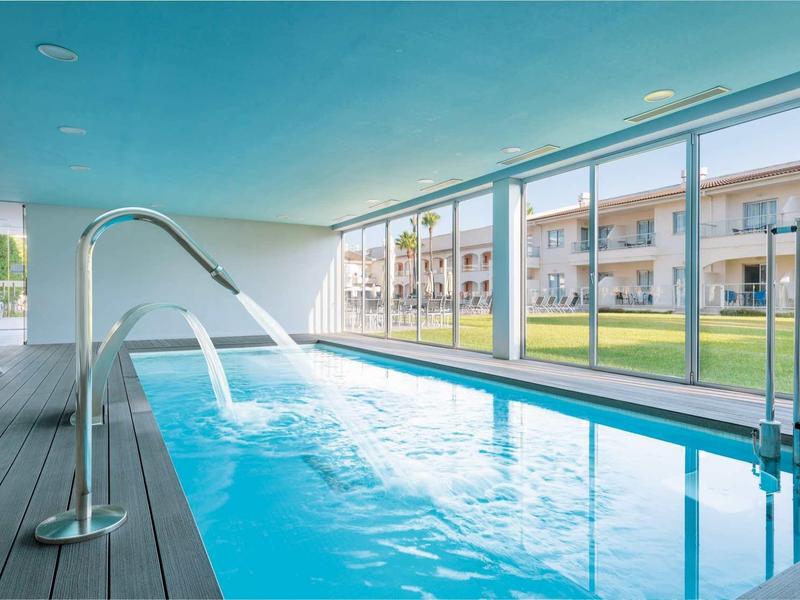 Kryty basen z dyszami wodnymi i dużymi oknami z widokiem na zielony ogród.