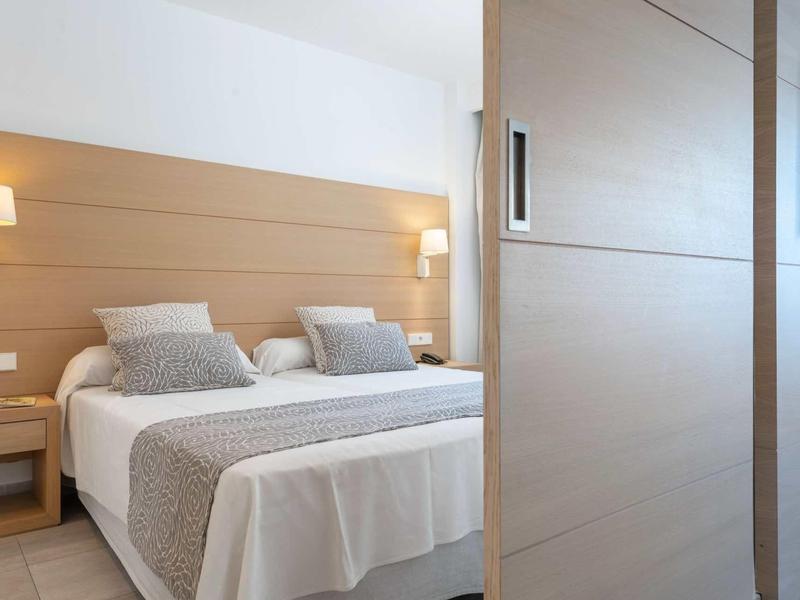 Nowoczesny pokój hotelowy z podwójnym łóżkiem, lampkami ściennymi i szafą przesuwaną.