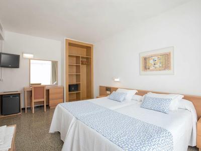 Chambre d'hôtel lumineuse avec deux lits, bureau, télévision et armoire ouverte.