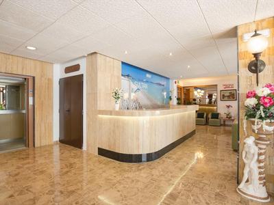 Hall d'hôtel lumineux avec réception, sol en marbre et décorations florales.