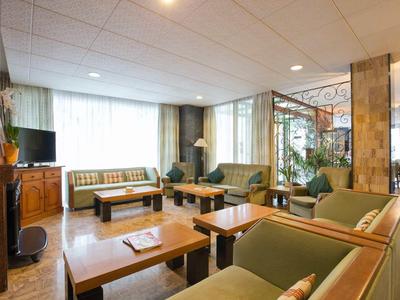 Salon d'hôtel confortable avec canapés, fauteuils, tables en bois, lumière naturelle et plantes.