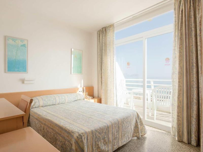 Chambre lumineuse avec lit double et accès à un balcon avec vue sur la mer.