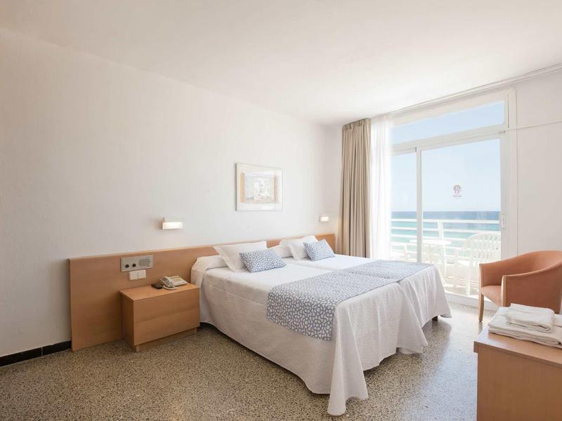 Chambre d'hôtel lumineuse avec lit double, balcon et vue sur la mer.