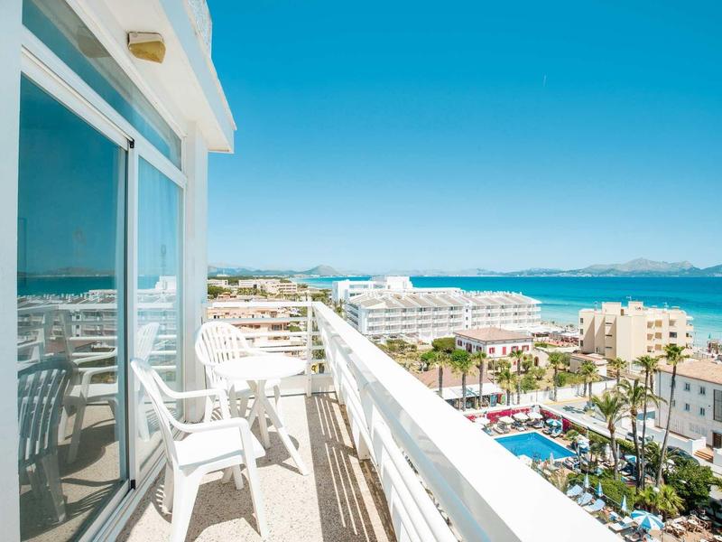 Balcon avec chaises blanches, vue sur la mer et piscine d'hôtel sous ciel clair