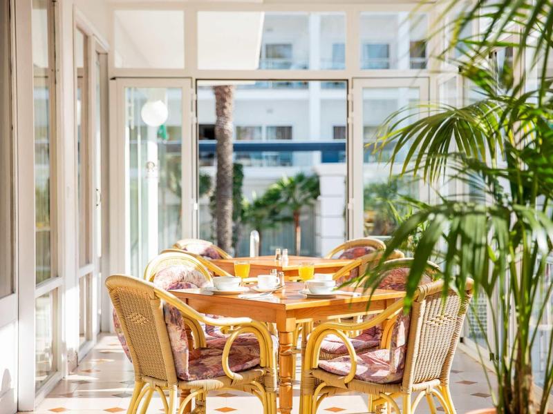 Véranda lumineuse avec chaises en osier et plantes, vue sur un espace extérieur ensoleillé.