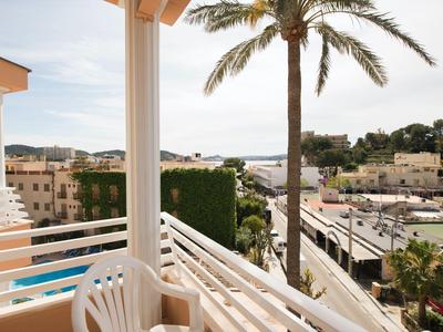 Balcony with white chairs overlooking palm trees, pool, and buildings in a sunny city.