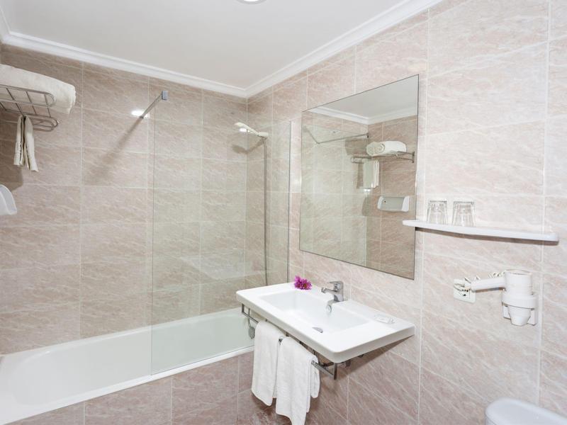 Bright bathroom with bathtub, sink, large mirror, and towels.
