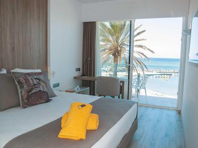 Camera d'hotel moderna con vista mare, letto con asciugamano giallo e balcone con palme.